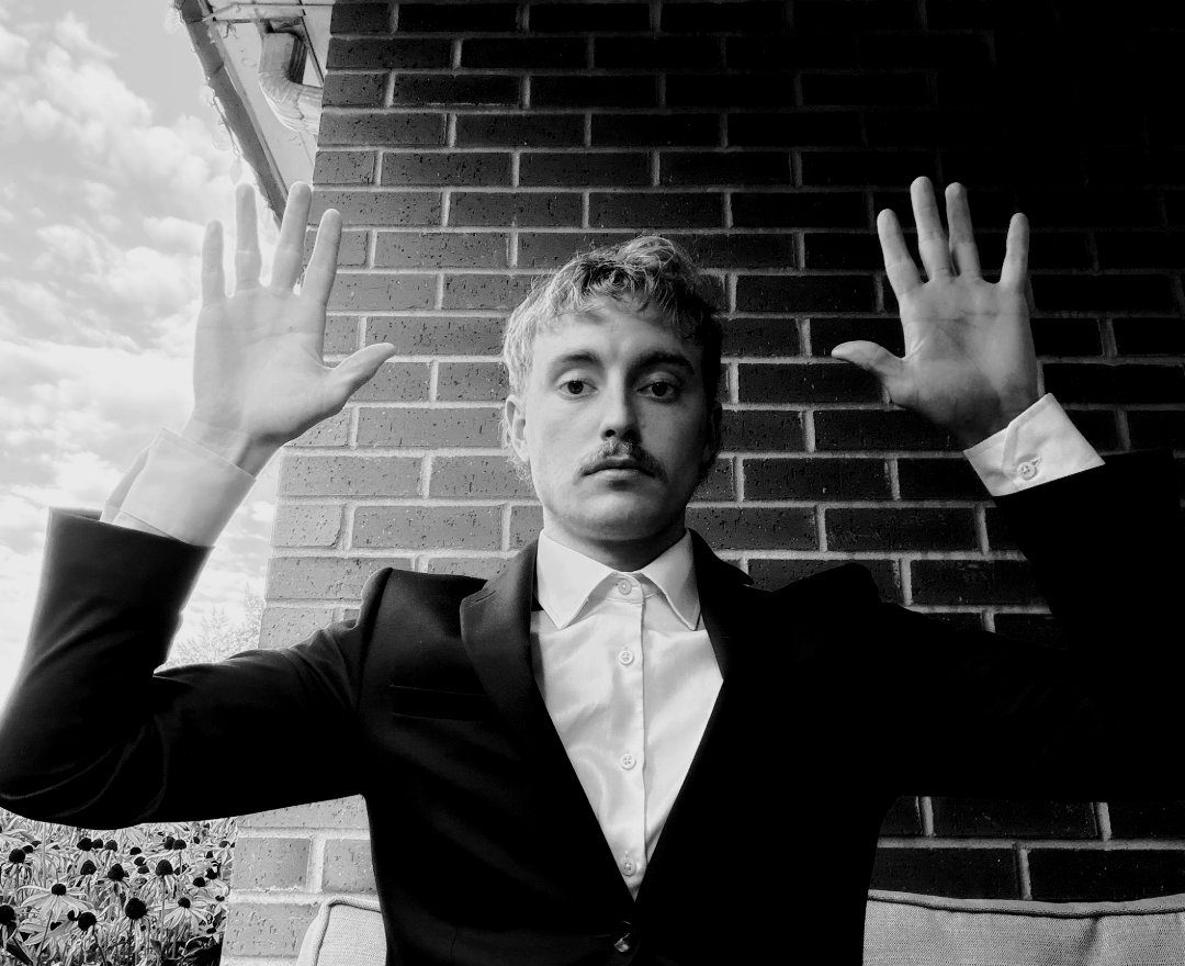 Black and white portrait of Chace Cade in a suit against a brick wall